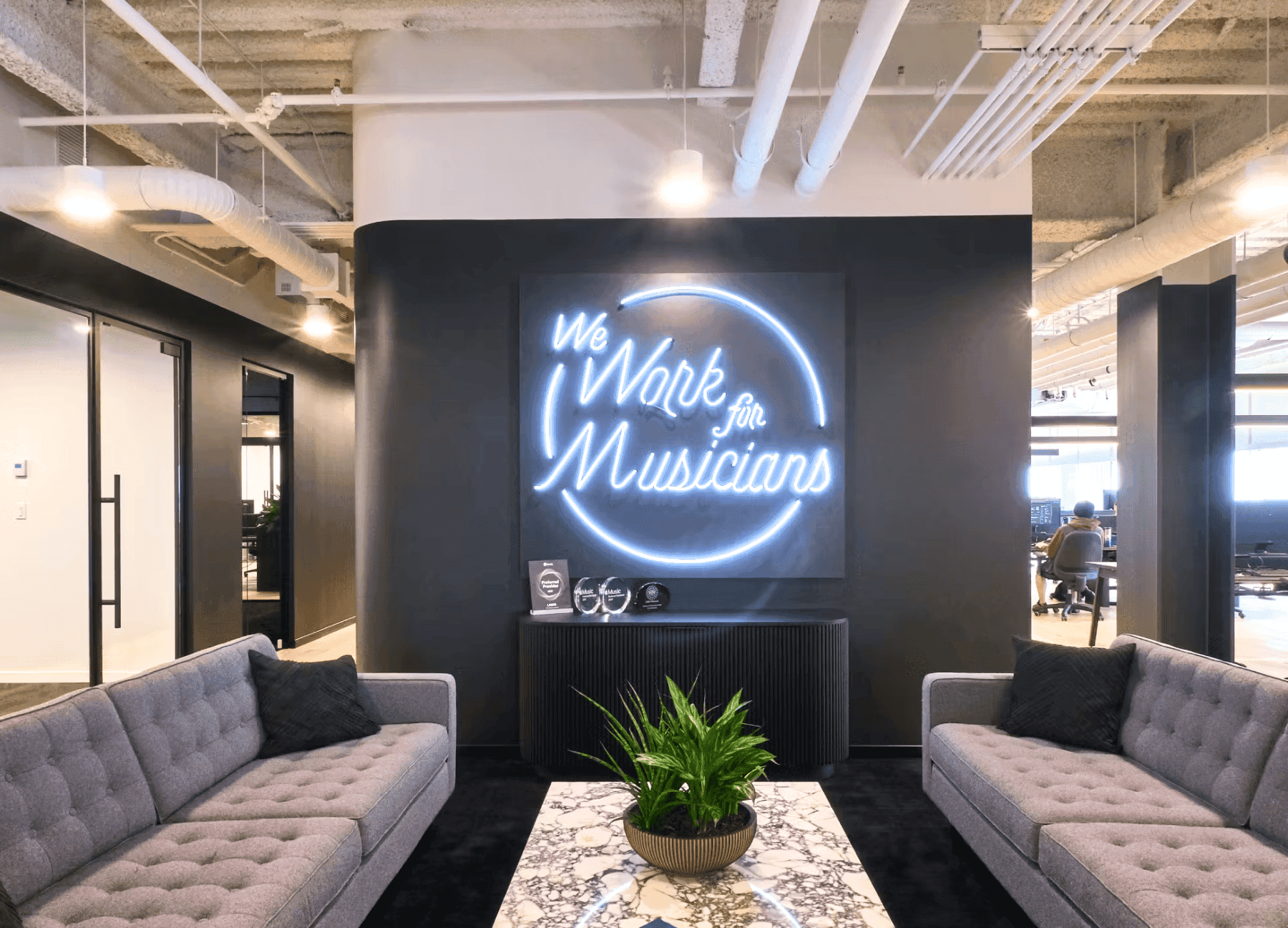 Stylish lounge with neon sign 'We Work for Musicians', dark sofa, and LANDR logo