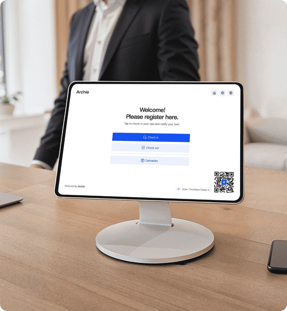 Reception tablet on wooden desk displaying Archie visitor registration screen with check-in buttons.