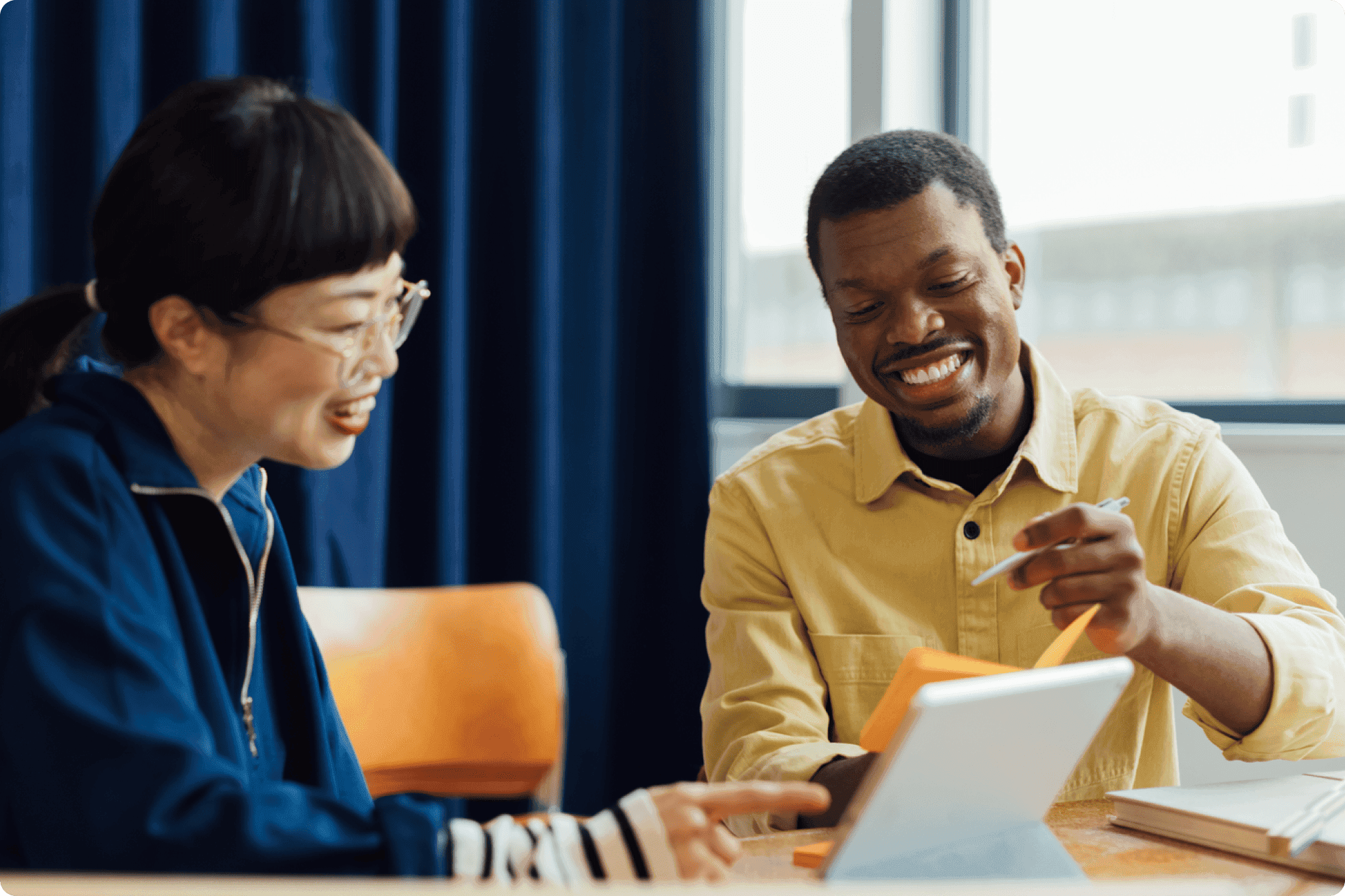 Two coworkers collaborating at table, pointing at digital tablet with notes and pens.