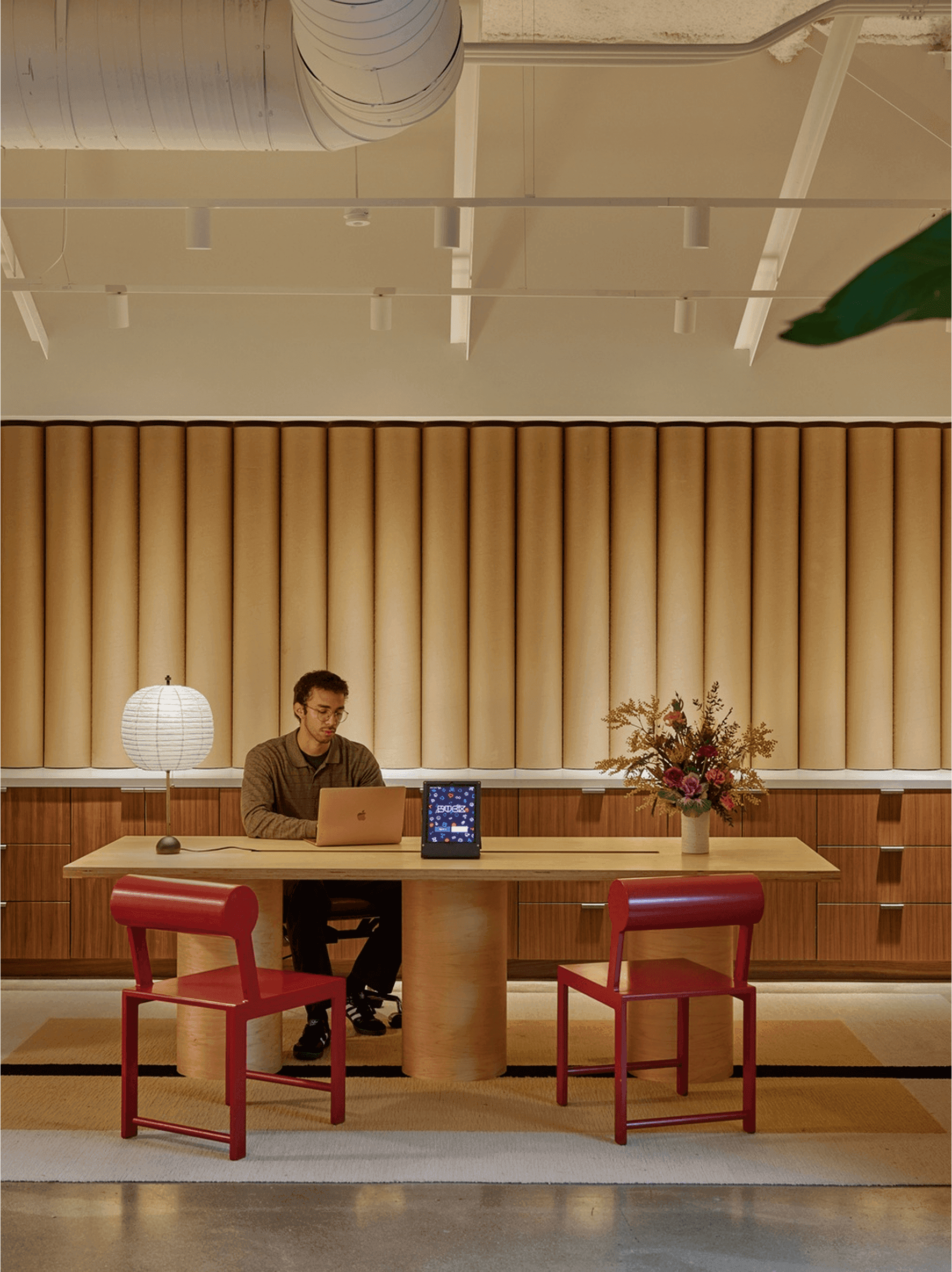 Un homme travaillant sur un ordinateur portable à un bureau en bois avec des chaises rouges dans un bureau moderne