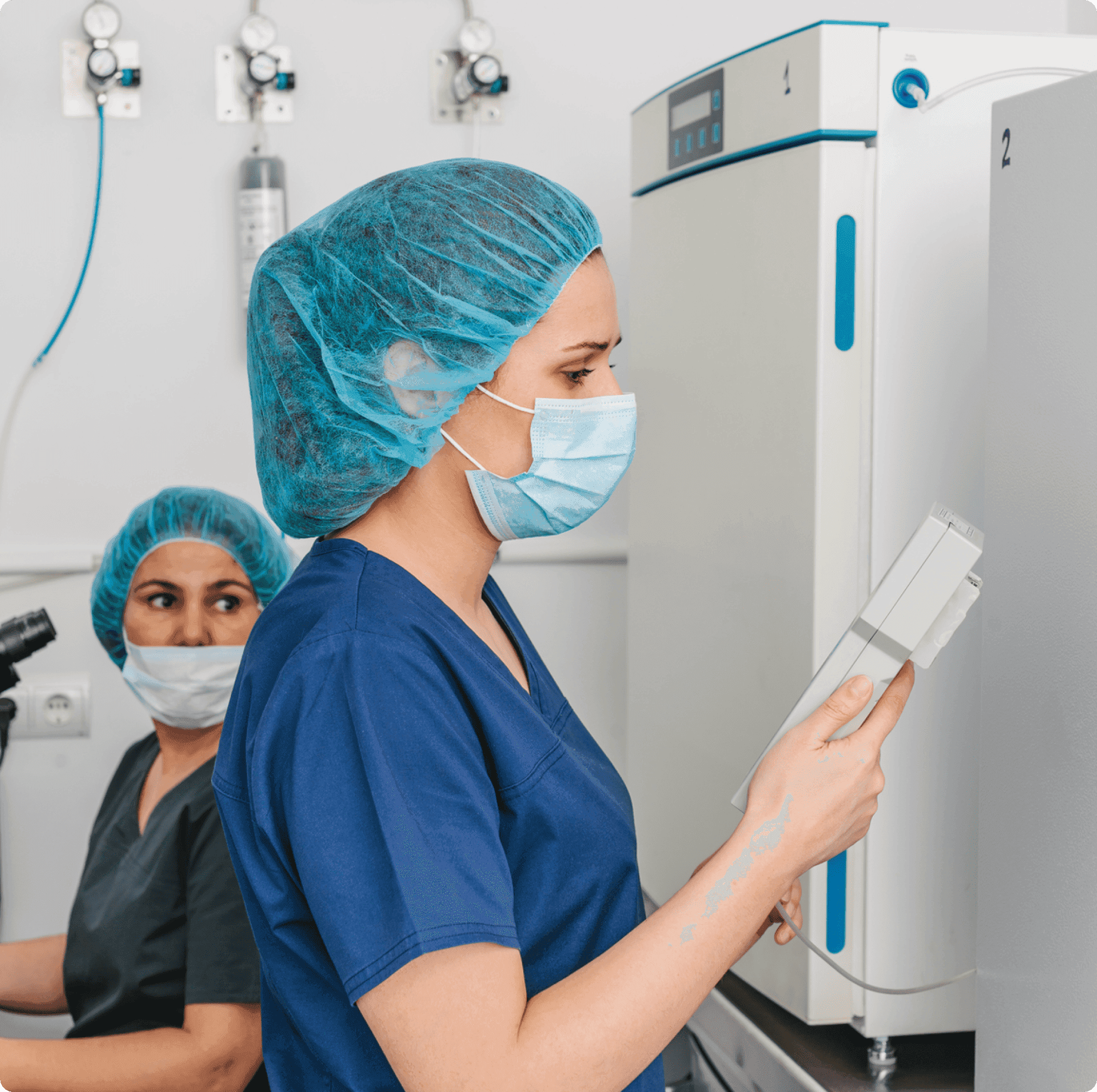 Healthcare workers in scrubs and hairnets working near medical equipment in a clinical setting