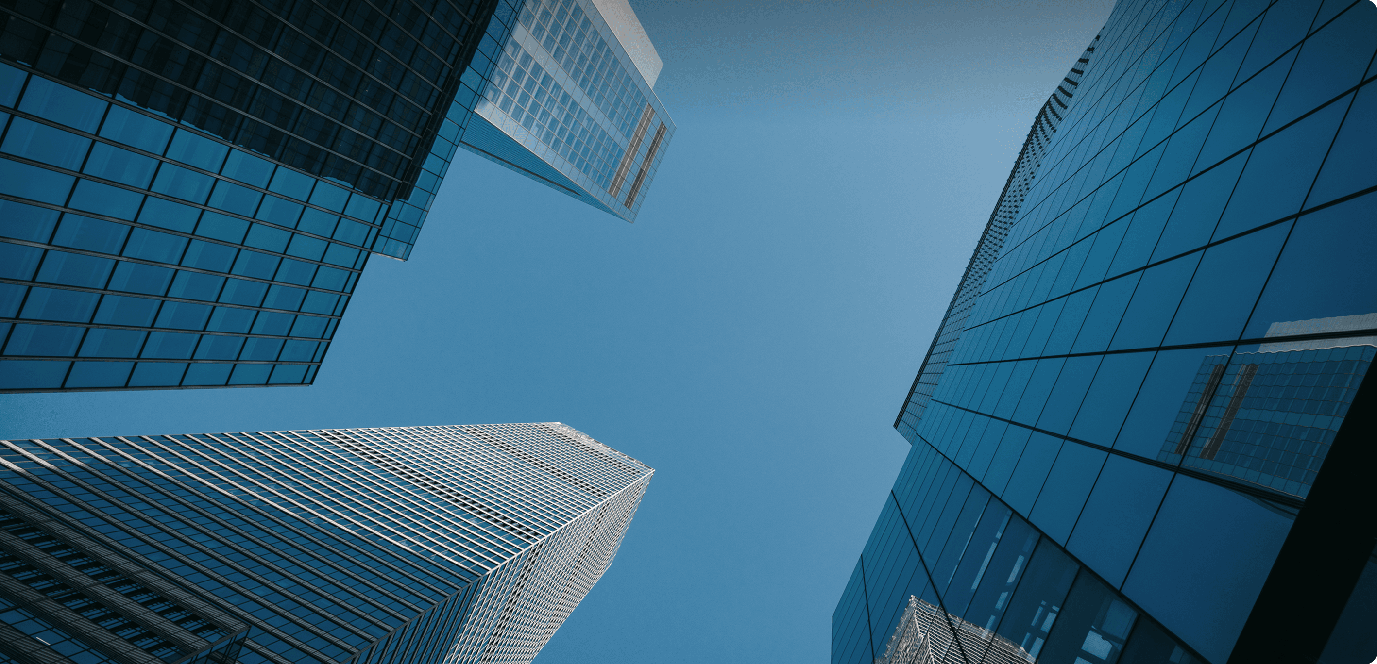 Upward view of tall, glass-covered office buildings under a clear blue sky