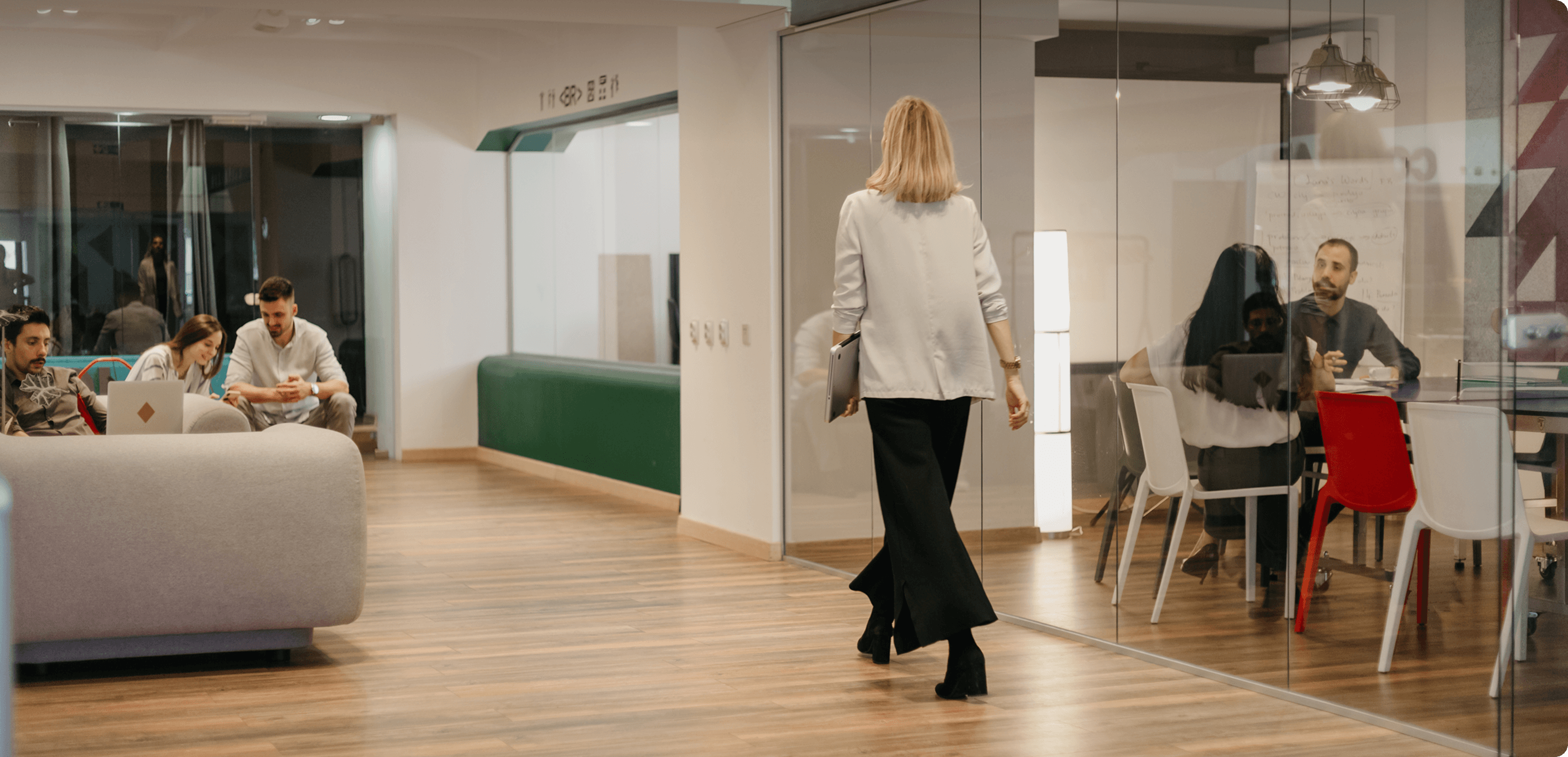 People working and walking in a spacious modern office with glass meeting rooms and wood flooring
