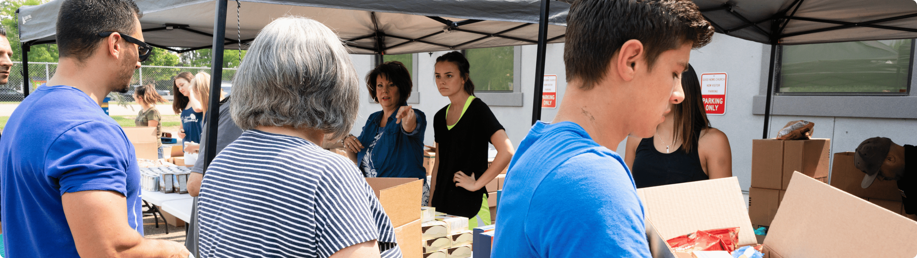Volunteers distribute food or supplies to people under tents at a community outdoor event.