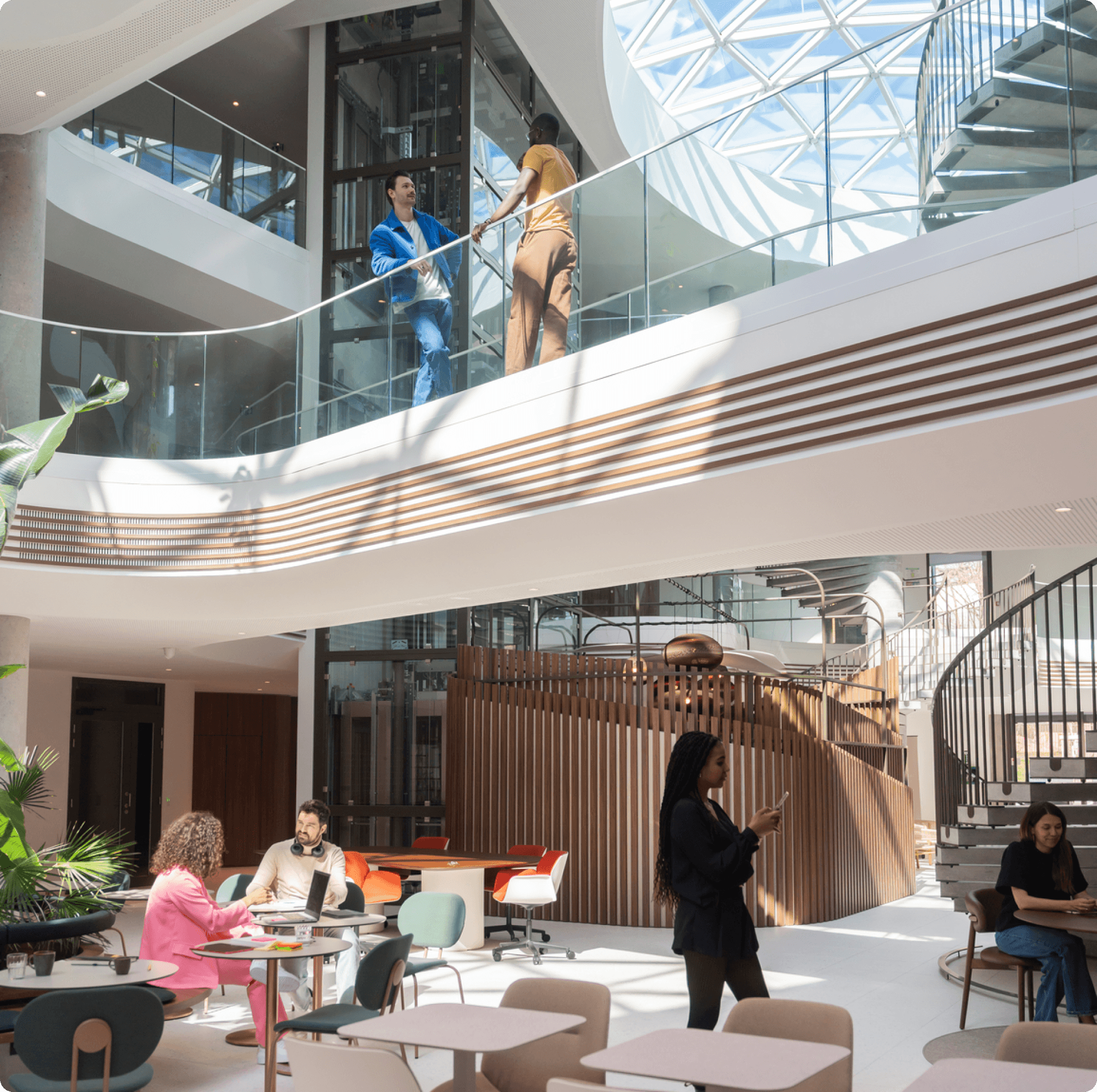 Modern atrium interior with a spiral staircase, skylight, people working at tables and walking