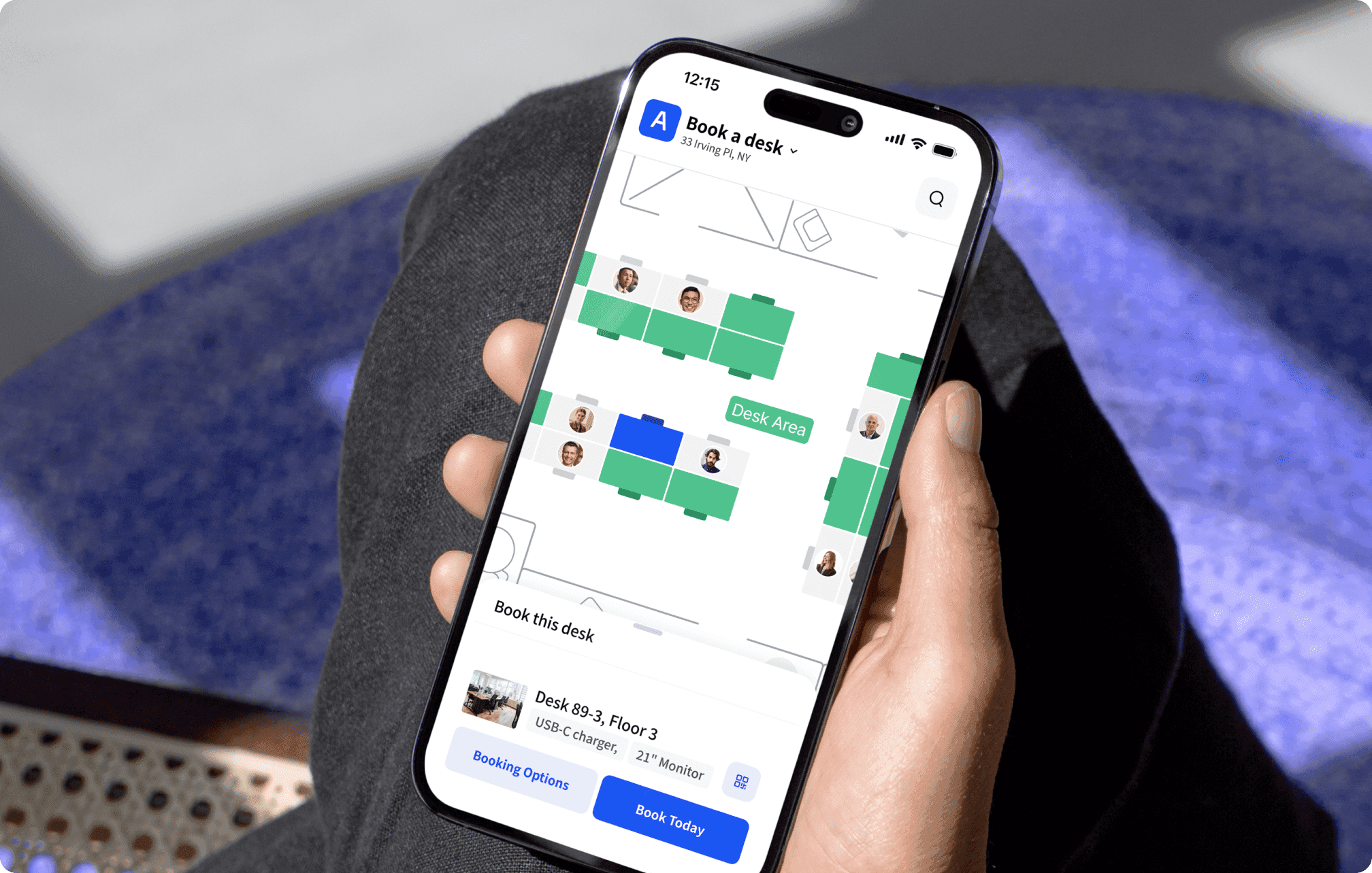 Phone held by hand showing “Book a desk” app with purple floor map highlighting available desks in green.