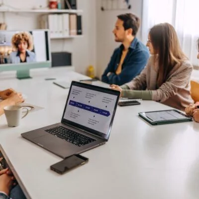 A group of people in a meeting room having a video conference with a colleague on a screen.