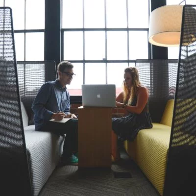 Two people collaborating in a modern office lounge area with a casual and inviting atmosphere.