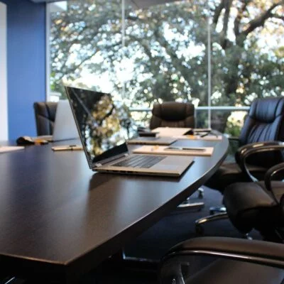 A modern conference room with a large, dark wooden oval table surrounded by black leather chairs with armrests.