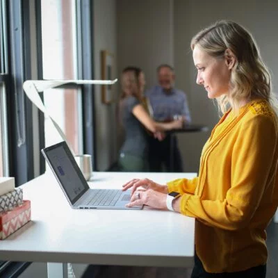 The image shows a woman standing at a desk in a modern office space.