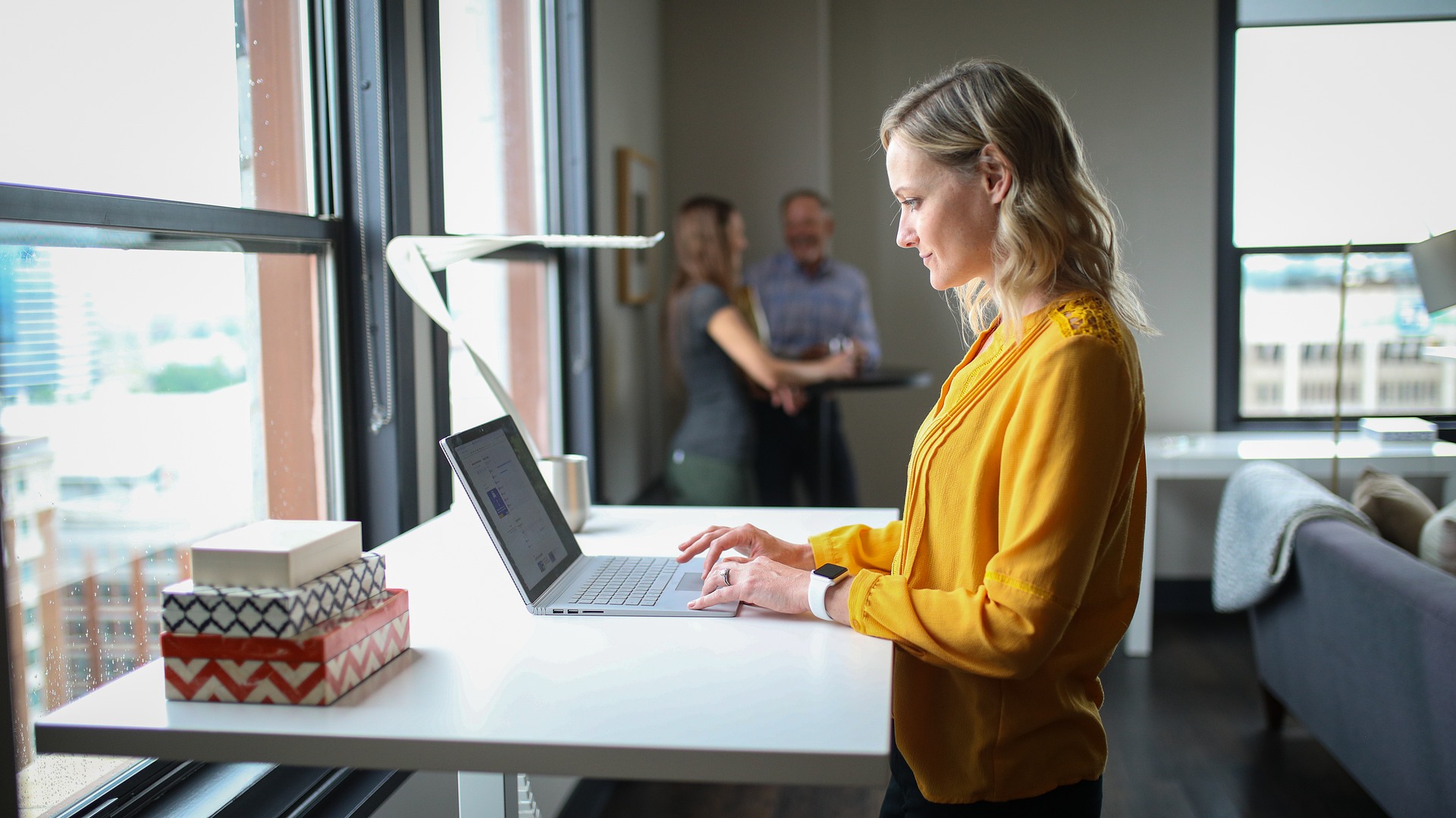 The image shows a woman standing at a desk in a modern office space.