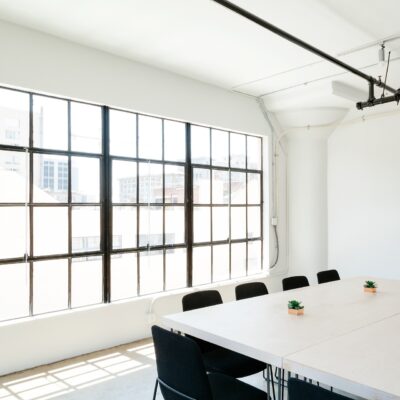 A bright and minimalist conference room with a large wooden table surrounded by black chairs.