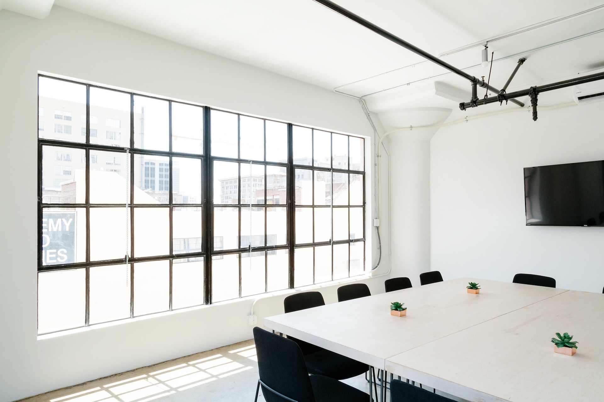 A bright and minimalist conference room with a large wooden table surrounded by black chairs.