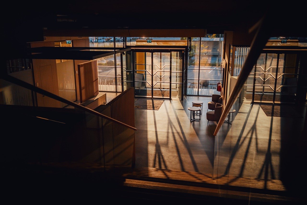 a modern office or lobby area with a warm and inviting ambiance created by natural sunlight streaming through large glass doors and windows.