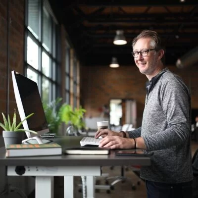 A man standing at a desk in a modern office space, using software to book a desk for the next day.