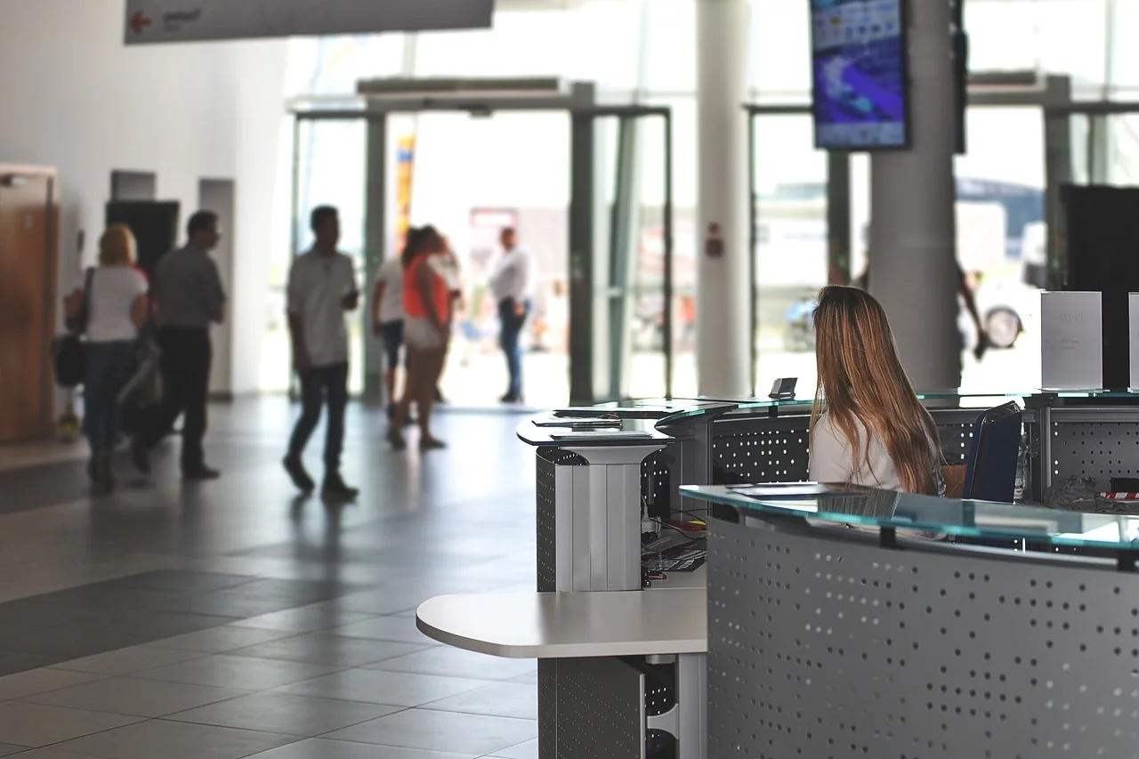 A reception area with a front desk on the right, where a woman is seated.