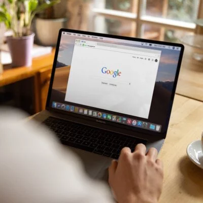 A person using a laptop with the Google homepage open on the screen.