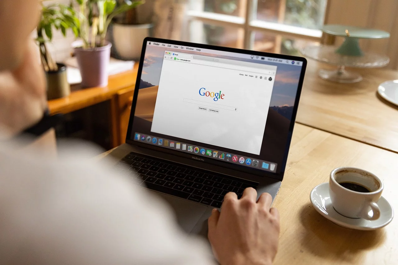 A person using a laptop with the Google homepage open on the screen.