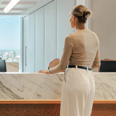 Person standing at a modern office reception desk with a city view in the background.
