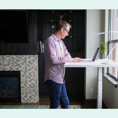 A man working at a laptop in a modern, open office space with other people in the background.