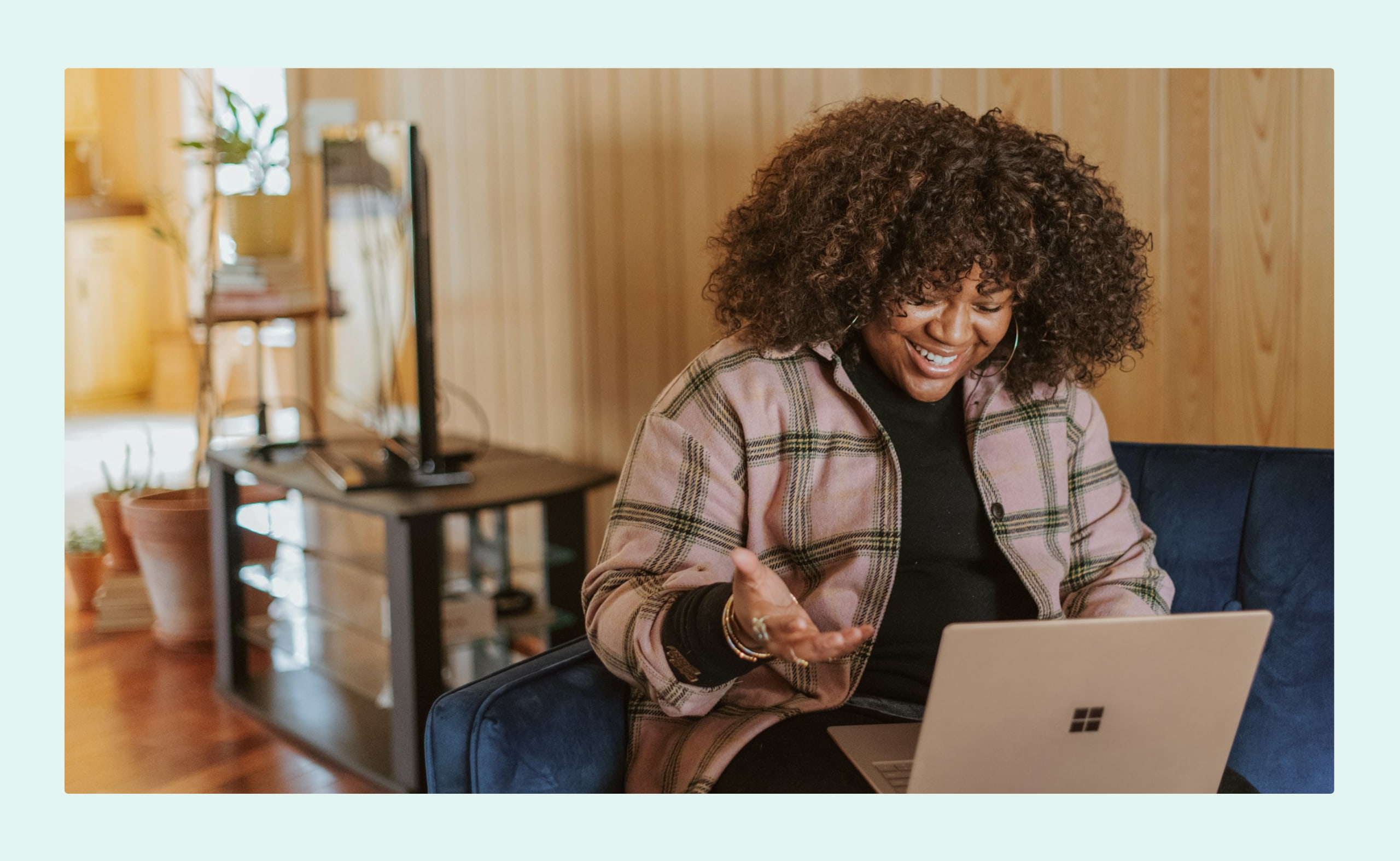 Smiling woman sitting on a couch, video chatting on her laptop in a cozy, wood-paneled room.