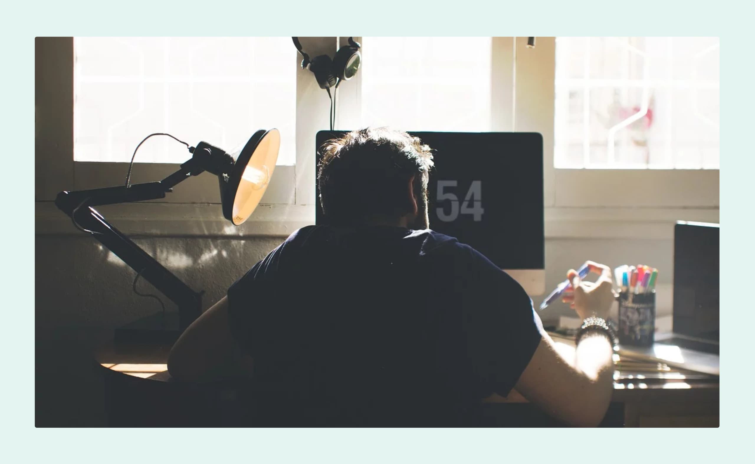 A person working at a desk in front of a computer, with sunlight coming through the window behind them.