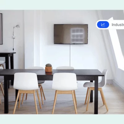 Minimalist meeting room with a long black table, white chairs, a wall-mounted TV, and a small potted plant.
