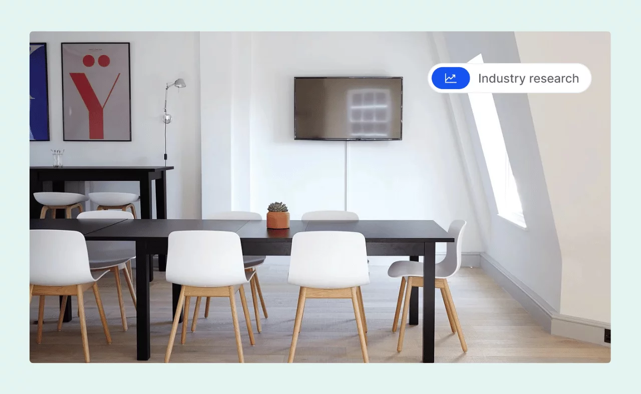 Minimalist meeting room with a long black table, white chairs, a wall-mounted TV, and a small potted plant.