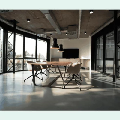 Modern meeting room with large windows, a wooden conference table, pink chairs, and industrial-style ceiling lighting.