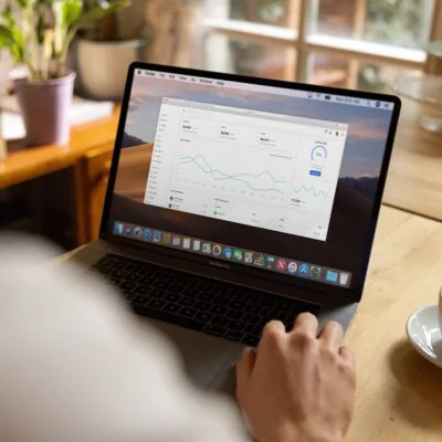 Person using a laptop at a wooden table with a cup of coffee, viewing a data dashboard on the screen.