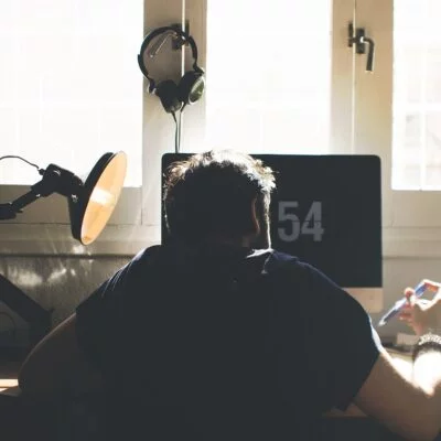 A person working at a desk in front of a computer, with sunlight coming through the window behind them.