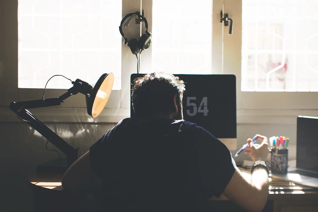 A person working at a desk in front of a computer, with sunlight coming through the window behind them.