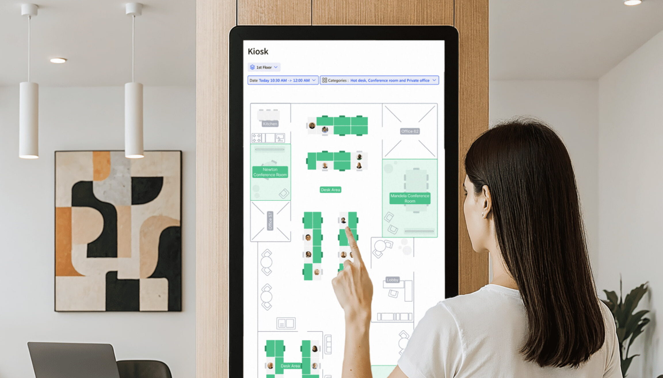 13+ Best (Hot) Desk Booking Software & Alternatives in 2026 A woman using a touchscreen kiosk to view a digital office floor plan and desk availability.