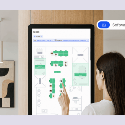 A woman using a touchscreen kiosk to view a digital office floor plan and desk availability.