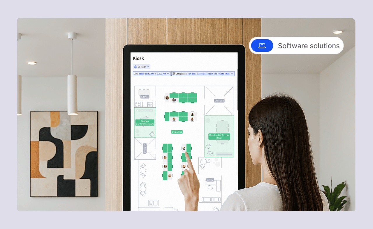 A woman using a touchscreen kiosk to view a digital office floor plan and desk availability.