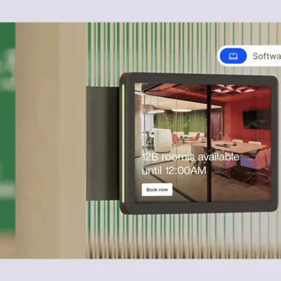 A digital room display panel showing a meeting room's availability and a “Book now” button.