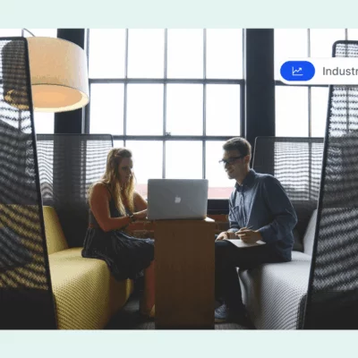 Two people sitting in a modern office lounge, working together on a laptop.