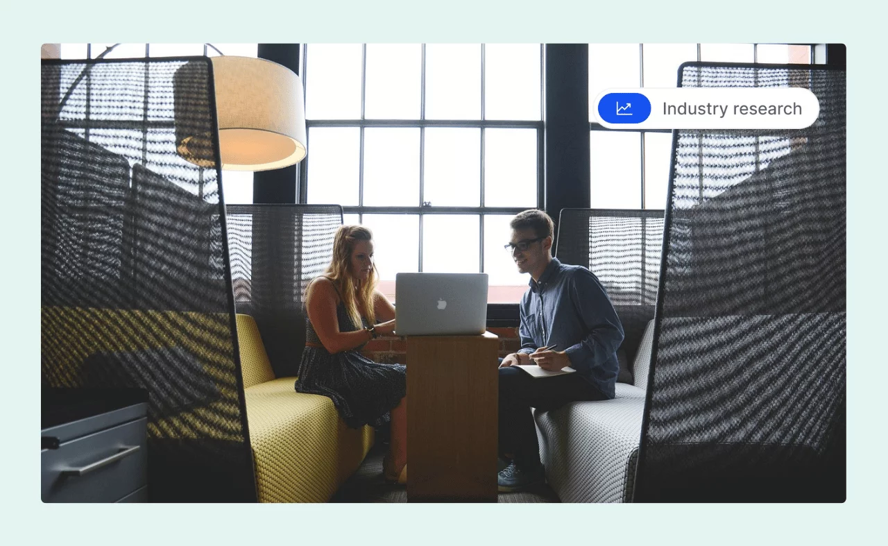Two people sitting in a modern office lounge, working together on a laptop.