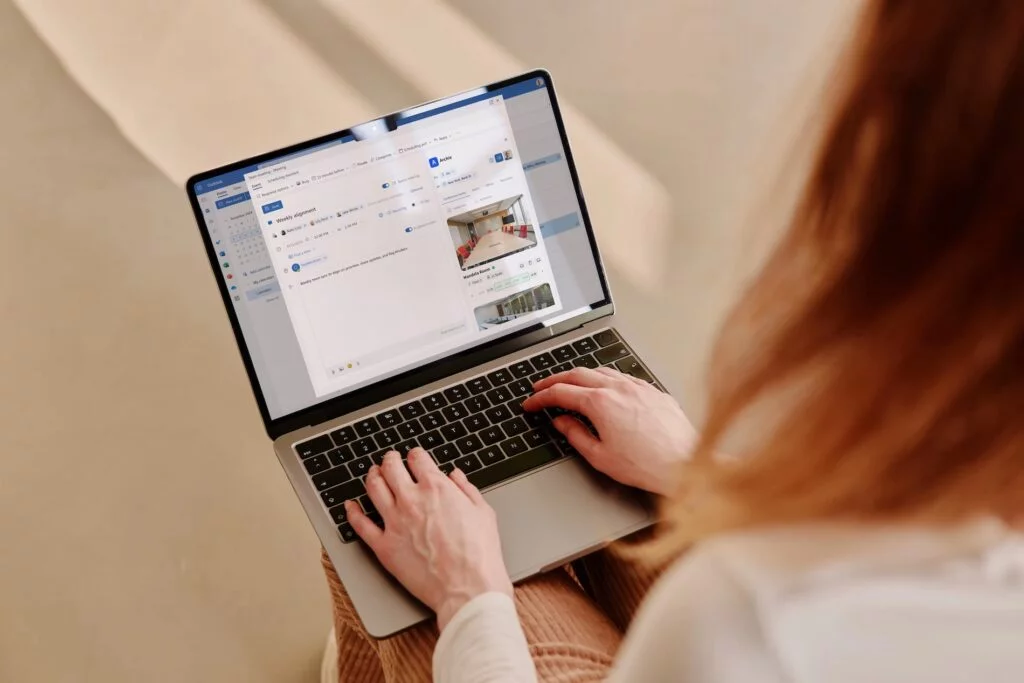 A person types on a laptop showing a meeting invitation in Outlook with a conference room booking via Archie.