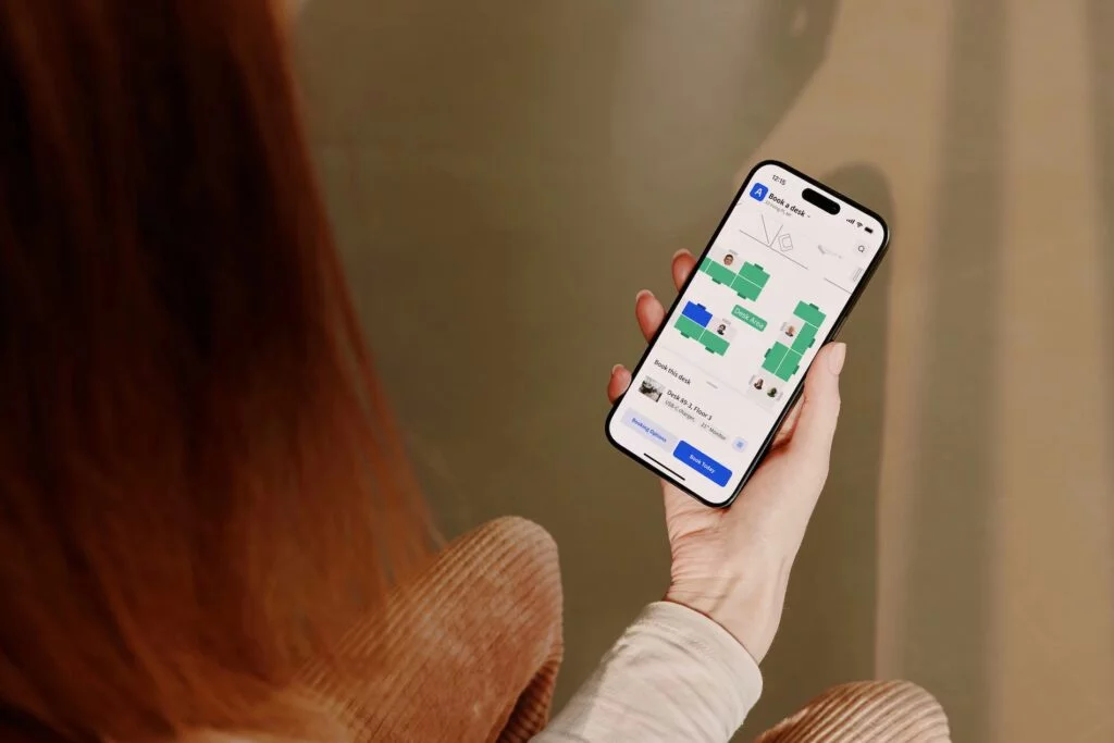 A person holds a phone displaying the Archie app for booking a desk in a floor plan view.