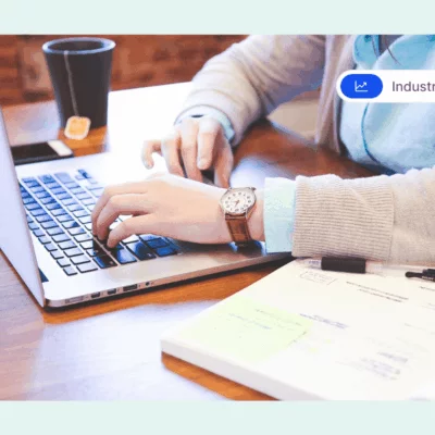A productive employee typing on a laptop at a desk with notes, a pen, and a cup of tea.