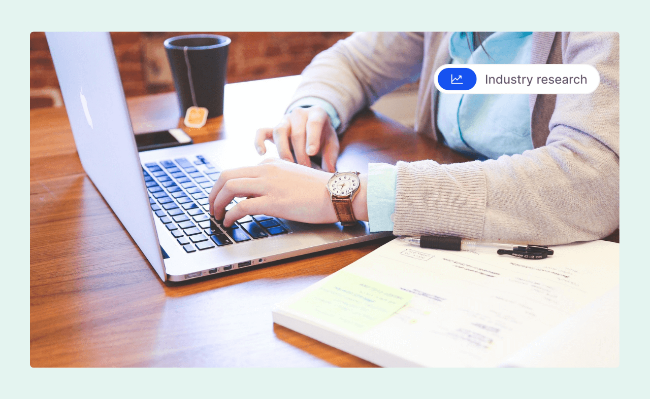 A productive employee typing on a laptop at a desk with notes, a pen, and a cup of tea.