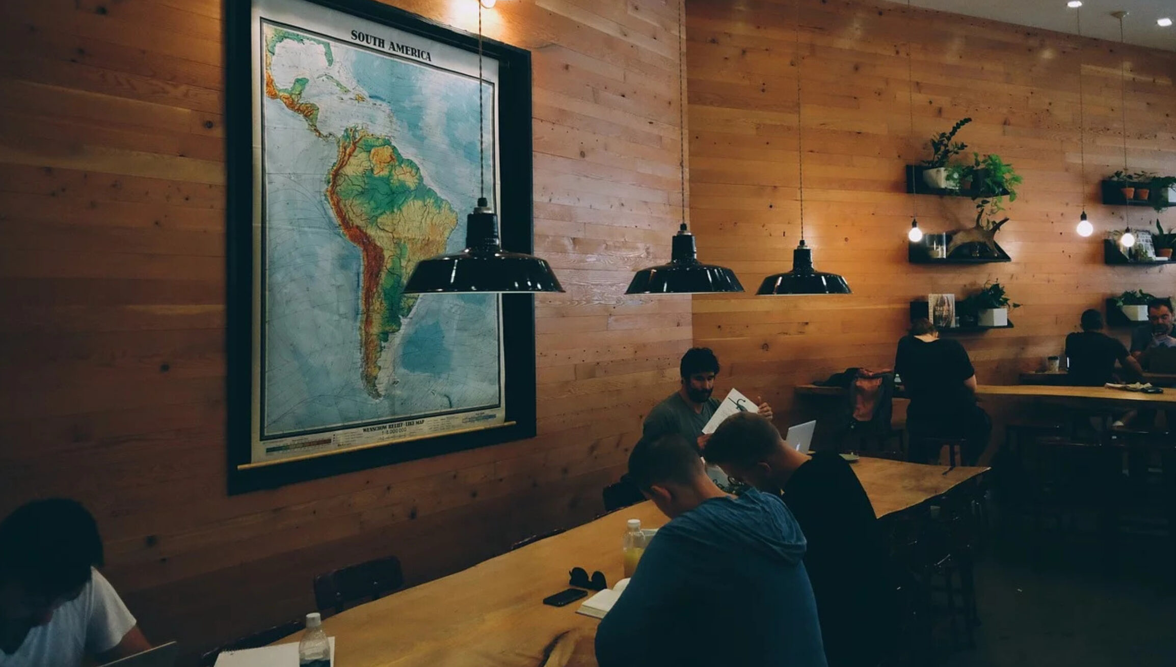 A cozy coworking space with wooden walls, warm lighting, and a large map of South America.