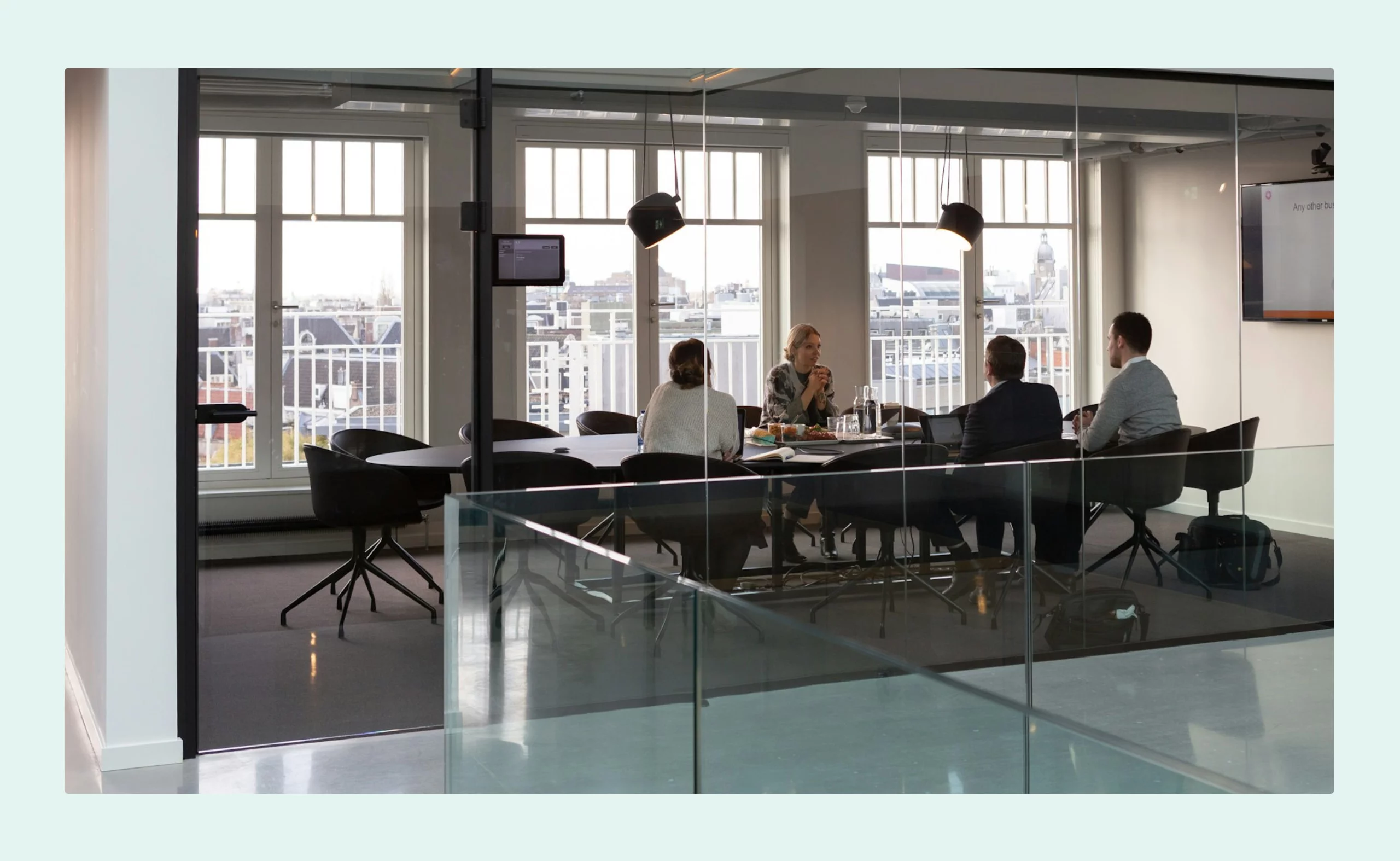 Four professionals in a glass-walled meeting room having a discussion, with city views in the background.
