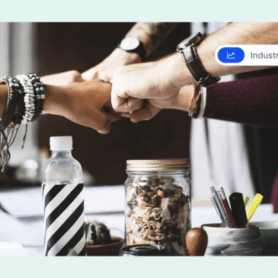 Four people doing a group fist bump over a desk, symbolizing teamwork and workplace collaboration.