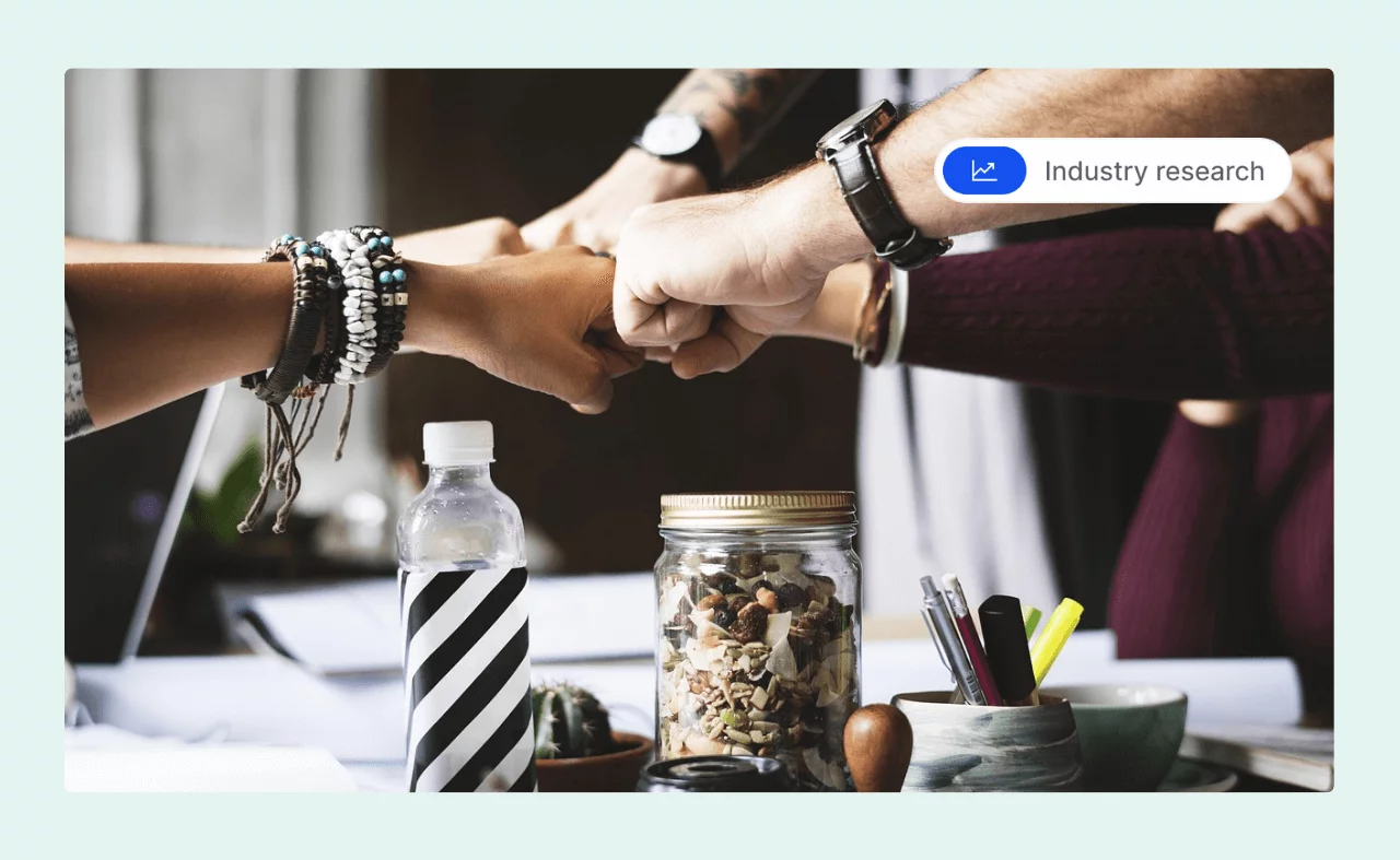 Four people doing a group fist bump over a desk, symbolizing teamwork and workplace collaboration.