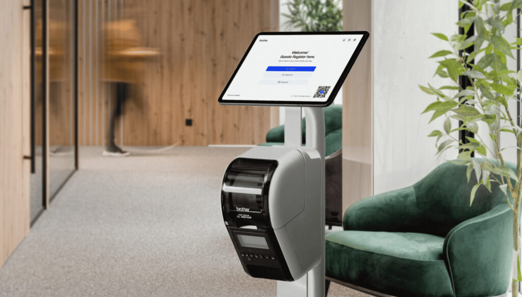 Quiosco digital de registro de Archie con pantalla táctil e impresora de tarjetas, instalado en el moderno vestíbulo de una oficina, en el que se muestra un formulario de registro de huéspedes.