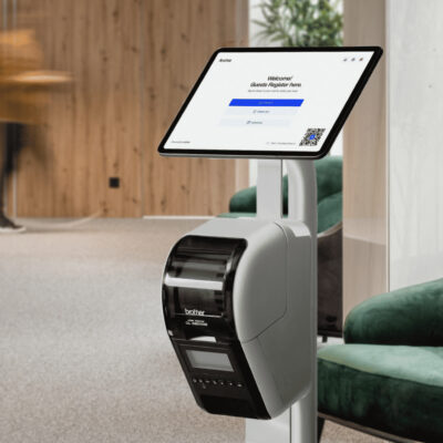 Archie's digital check-in kiosk with a touchscreen and badge printer set up in a modern office lobby, displaying a guest registration form.