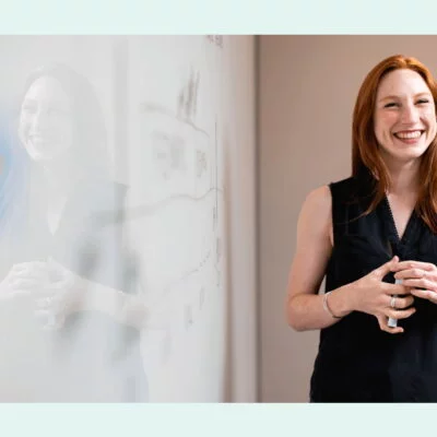 Smiling woman standing next to a whiteboard during a presentation or team meeting in a modern office.
