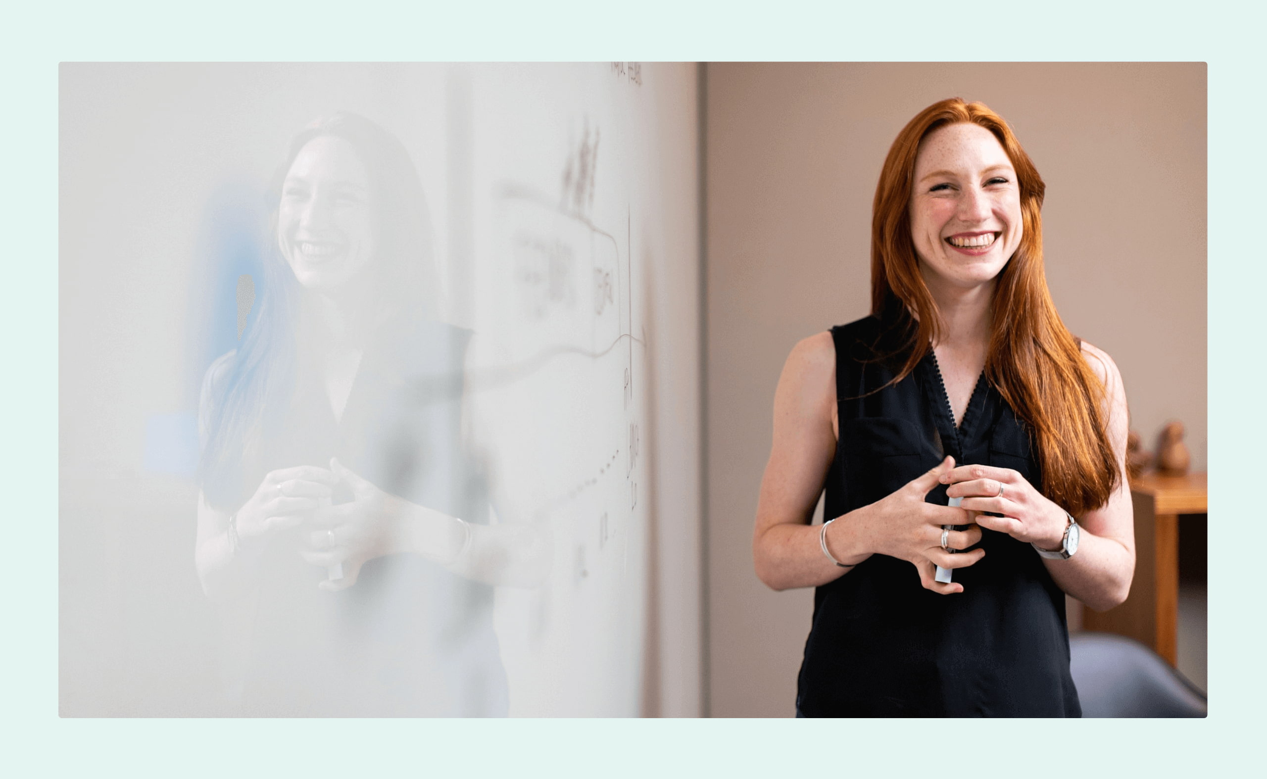 Smiling woman standing next to a whiteboard during a presentation or team meeting in a modern office.